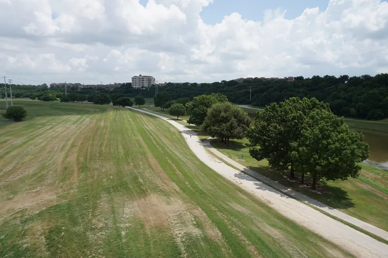 A paved trail curving through green parkland along the Trinity River in Fort Worth